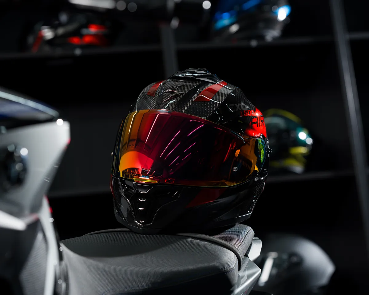 Scorpion EXO-1500 Air carbon met rood iridium vizier op het zadel van een motor in de Vespucci-showroom